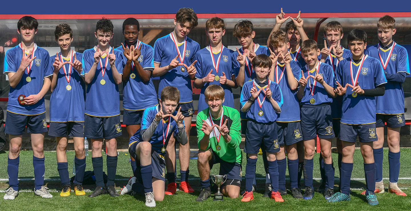 A boys' football team posing with medals and a cup after winning a competition