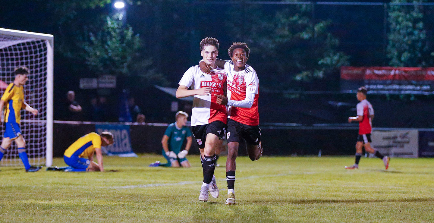 Two Woking FC Academy players running together on pitch and celebrating a goal