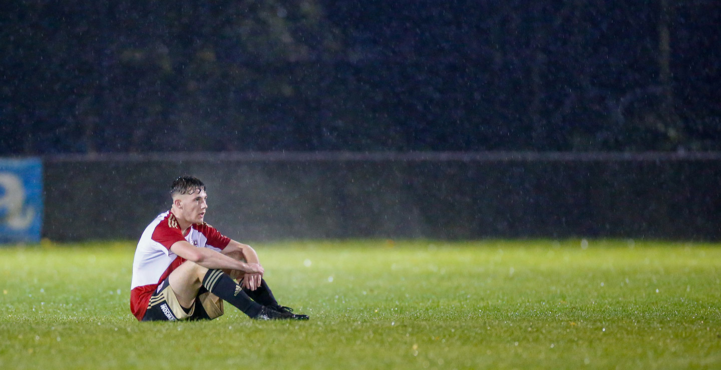 A Woking FC Academy player sitting on a pitch in the rain