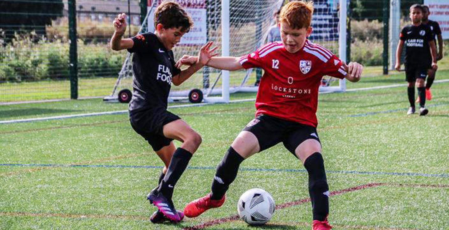 A pre-academy Woking player and opposing player challenging for the football.